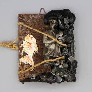Peut inclure: Une décoration murale rectangulaire composée d'une plaque métallique rouillée avec un poisson jaune peint, une figurine argentée en manteau et une matière noire texturée avec des éclats de verre, le tout lié par une ficelle beige.