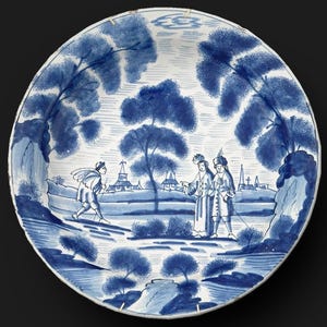 May include: A blue and white ceramic plate with a landscape scene. The plate features a detailed illustration of figures, trees, and buildings. The design is in a traditional style, with a focus on the blue and white color scheme.
