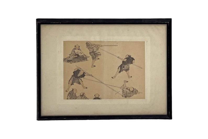 May include: Framed black and white print depicting several figures engaged in a martial arts practice. The artwork features multiple figures in dynamic poses, wielding long weapons. The print is set against a cream-colored background.