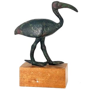 Peut inclure: Une sculpture d'oiseau en bronze avec un long bec incurv&eacute;, pos&eacute;e sur un bloc de bois. L'oiseau pr&eacute;sente une patine vert fonc&eacute; avec des reflets rouges. La sculpture est un objet d&eacute;coratif.