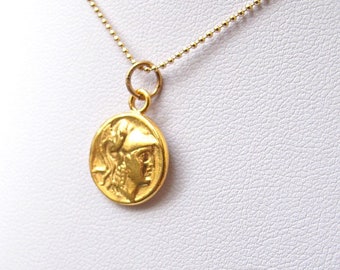 May include: A gold chain necklace with a round pendant featuring a profile of a woman wearing a helmet. The pendant is a replica of an ancient Greek coin.
