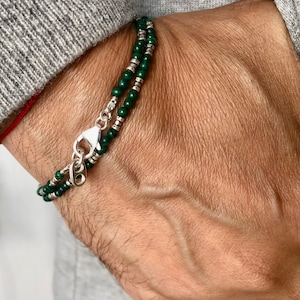 Puede incluir: Un brazalete de doble cadena con cuentas verdes y plateadas. El brazalete tiene un cierre plateado.