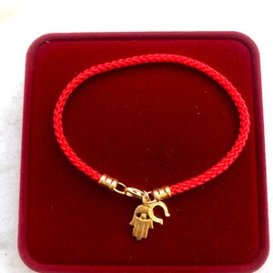 May include: Red string bracelet with a gold charm featuring a hamsa hand with an evil eye and a horseshoe.