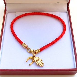 May include: Red string bracelet with a gold charm featuring a hamsa hand and horseshoe. The bracelet is in a red velvet box.