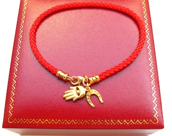 May include: A red string bracelet with a gold charm featuring a hamsa hand and a horseshoe. The bracelet is displayed in a red velvet box.