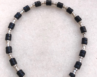 Peut inclure: Un bracelet composé de perles cylindriques noires et de maillons en métal argenté. Le bracelet est doté d'un fermoir mousqueton. Les perles sont espacées de manière uniforme, créant un design simple et élégant. Le bracelet mesure environ 18 cm de long.