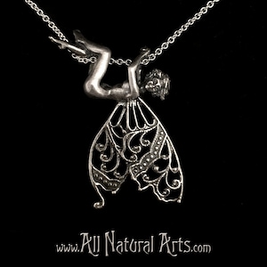 May include: A silver pendant necklace featuring a detailed fairy figurine with wings. The fairy is hanging upside down from the chain, with its wings spread out behind it.