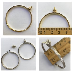 Pode incluir: Dois molduras de moedas douradas com um botão decorativo no topo. As molduras têm um diâmetro de 10 cm. Uma moldura está aberta e a outra está fechada.