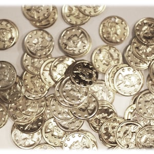 May include: A large pile of gold-colored metal tokens with intricate designs. The tokens are scattered on a white surface.