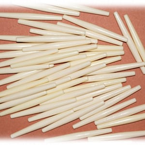 May include: A pile of off-white, smooth, cylindrical beads. The beads are about 1 inch long and have a slightly pointed end.