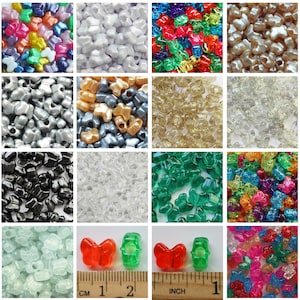 May include: A collection of colorful butterfly-shaped beads in various colors, including red, green, and blue. The image also shows a ruler with centimeter and inch measurements, with the beads measuring approximately 1 inch (2.5 cm) in length.