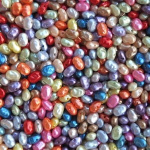 Może przedstawiać: Duża kolekcja kolorowych, perłowych, owalnych koralików. Koraliki są ułożone w losowym wzorze i mają różne rozmiary i odcienie.