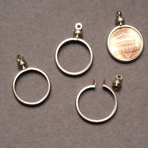 May include: Four silver coin bezel pendants, three are closed and one is open. The pendants have a small loop at the top for attaching to a chain or cord. One of the pendants is attached to a copper penny.
