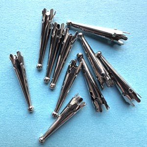 May include: A collection of shiny, silver-colored metal cone-shaped findings. Each piece has a rounded base and a flared, multi-pronged top. The findings are scattered on a light blue surface.