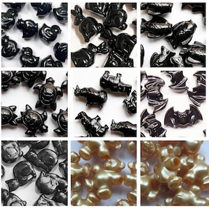 May include: A collection of small, glossy black animal figurines, including ducks, rabbits, fish, turtles, bats, and rhinos. Also, a group of gold-colored teddy bear figurines. The figurines are arranged on a white surface.