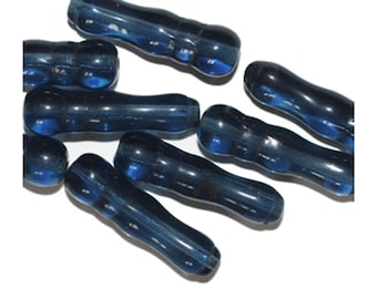 May include: A group of seven dark blue glass beads with a textured surface. The beads are shaped like long, thin cylinders with a slight bulge in the middle.