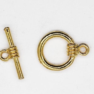 May include: Gold-toned metal toggle clasp with a round ring and a bar with a small loop. This clasp is used for necklaces, bracelets, and other jewelry.