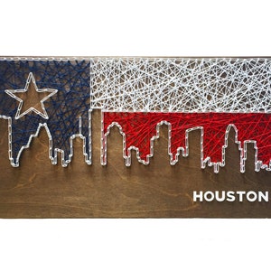 May include: String art depicting the Houston skyline against a backdrop of the Texas flag. The skyline is outlined in white string, and the flag is crafted with red, white, and blue string. The word "HOUSTON" is written in white letters at the bottom of the artwork.