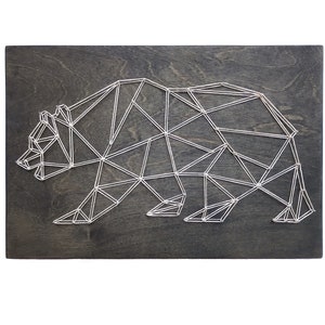 May include: A geometric bear design created with white string wrapped around nails hammered into a dark wood board.