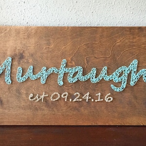 May include: A wooden sign with the name "Murtaugh" spelled out in blue string art. The date "est 09.24.16" is written below the name in white string art.