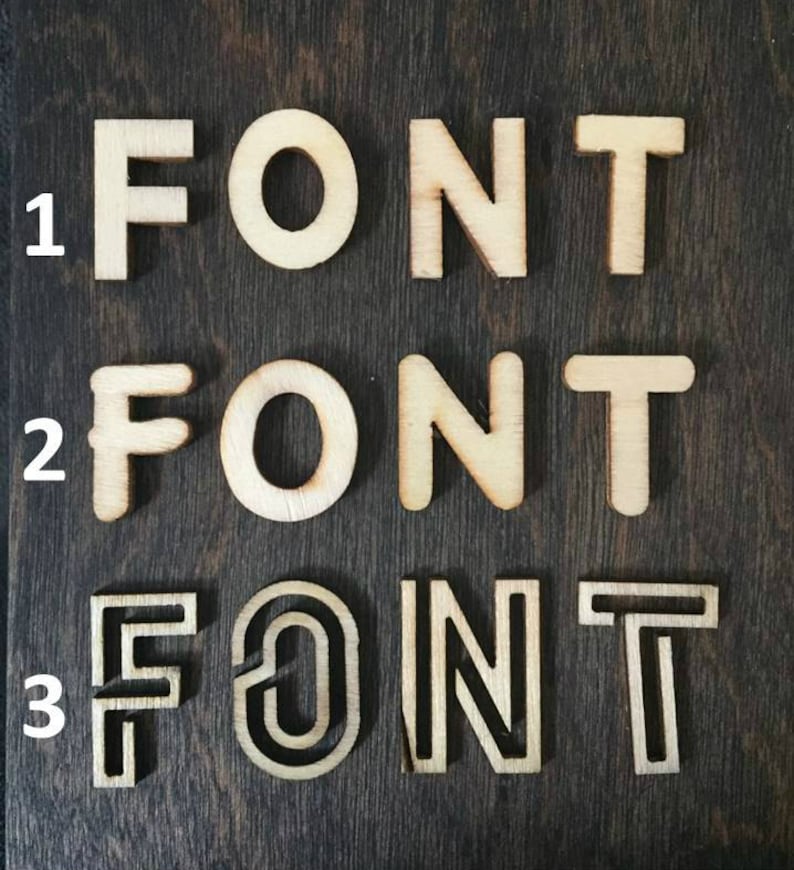 K&ouml;nnte beinhalten: Drei verschiedene Stile des Wortes "FONT" aus Holz ausgeschnitten. Der erste Stil ist eine einfache, klobige Schriftart. Der zweite Stil ist eine leicht abgerundete Schriftart. Der dritte Stil ist eine dekorativere Schriftart mit einer doppelten Umrandung.