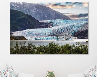 May include: A rectangular wall art print featuring a landscape photograph of a blue glacier nestled between dark mountains, displayed above two white armchairs with patterned cushions, a wooden side table, and a potted green tree.