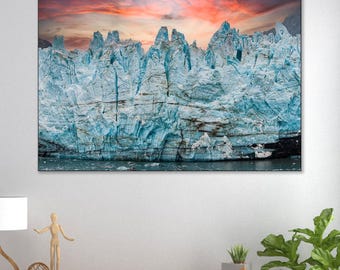 May include: A rectangular wall art print featuring a massive, jagged glacier with deep blue ice crevices and sharp peaks under a vibrant sunset sky with streaks of orange, pink, and red clouds, displayed above a light brown wooden sideboard cabinet.