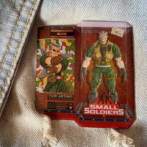 May include: A red, white, and blue box with a cartoon soldier on the front. The box says "Commando Elite" and "Small Soldiers". The soldier is holding a gun and has a green camouflage uniform.