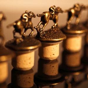 May include: A row of six gold bottle stoppers with a horse and rider design. The stoppers are made of metal and have a cork base.