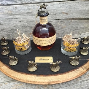 May include: A wooden barrel-shaped serving tray with a black finish. The tray features a bottle of Blanton's Original Single Barrel Bourbon Whiskey, two glasses, and eight miniature gold-colored horse figurines. The tray is perfect for serving drinks and snacks.