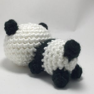 May include: A handmade crochet panda bear toy. The panda is white with black accents, including the ears, paws, and a stripe across the back. The toy is lying down, showcasing its soft, textured appearance.