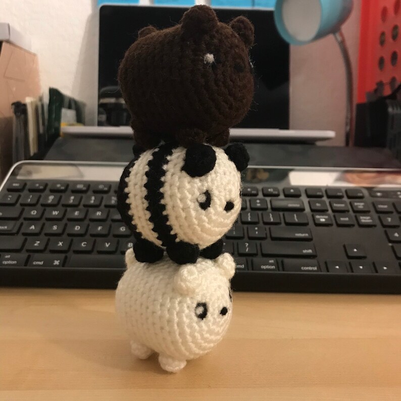 May include: A stack of three crocheted animal figures: a brown bear on top, a black and white panda in the middle, and a white bear at the bottom. Each figure has small black eyes and is made of yarn.