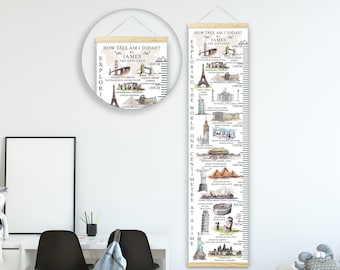 Puede incluir: Un gráfico de crecimiento blanco y beige con una varilla de madera en la parte superior. El gráfico presenta una ilustración colorida de monumentos famosos de todo el mundo, incluyendo la Torre Eiffel, la Estatua de la Libertad y la Gran Muralla China. El gráfico está etiquetado como "¿Qué altura tengo hoy?" y "Explorando el mundo un centímetro a la vez."