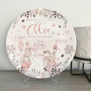 Op de afbeelding: Decoratieve plaat met een aquarelontwerp. Het toont twee konijntjes, bloemmotieven en de tekst "Welcome to the world little one Chloe Marie Fessenden." Bevat geboortedetails: 51.51 cm, 3.68 kg en de datum 22 oktober 2019.
