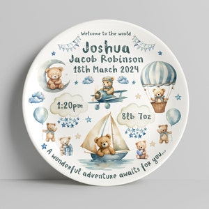 Puede incluir: Un plato de cerámica blanco con un diseño de acuarela azul y marrón con osos de peluche, un globo aerostático, un velero, un avión y estrellas. El plato incluye el texto "Welcome to the world Joshua Jacob Robinson 18th March 2024 1:20pm 8lb 7oz A wonderful adventure awaits for you..."