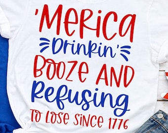 May include: White t-shirt with red and blue text that reads 'Merica Drinkin' Booze And Refusing To Lose Since 1776'.
