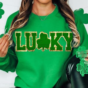 May include: Green sweatshirt with gold glitter lettering that says "LUCKY" with a green shamrock in the middle of the word.