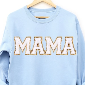 May include: Light blue sweatshirt with the word "MAMA" in white letters outlined in gold glitter.