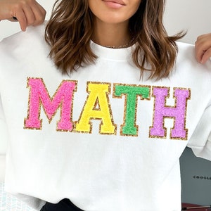 May include: White sweatshirt with the word "MATH" in large, colorful, fuzzy letters. The letters are outlined in gold glitter.