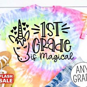 Op de afbeelding: Een tie-dye T-shirt met een eenhoorn en de tekst "1st Grade is magical".