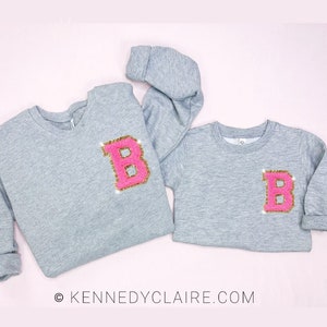 May include: Two gray sweatshirts with a pink and gold letter "B" on the front. The sweatshirts are on a light pink background. © KENNEDYCLAIRE.COM