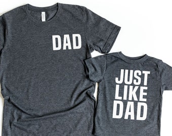 May include: Two gray t-shirts with white text. The larger shirt says "DAD" on the front. The smaller shirt says "JUST LIKE DAD" on the back.