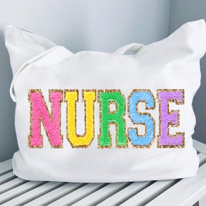 May include: White canvas tote bag with the word "NURSE" spelled out in colorful, glittery letters. The letters are outlined in gold.