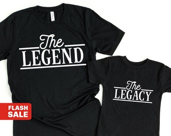May include: Two black t-shirts with white text. The larger shirt says "The Legend" and the smaller shirt says "The Legacy".