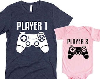 May include: A set of two t-shirts, one navy blue and one pink, with a video game controller graphic and the text "Player 1" and "Player 2".