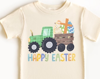 May include: A light beige t-shirt featuring a green tractor carrying a lamb and Easter eggs. The tractor has a wooden bed and the eggs are decorated with colourful patterns. The text "HAPPY EASTER" is printed in rainbow colours below the tractor.