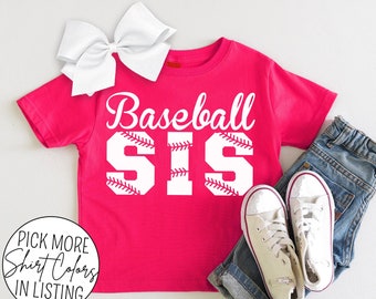 Può includere: Maglietta rosa a tema baseball con testo bianco che dice "Baseball Sis" con una grafica di baseball in ogni lettera.