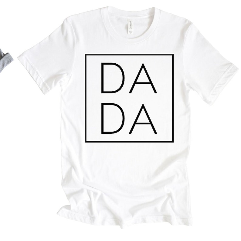 Puede incluir: Camiseta blanca con un cuadrado negro que contiene el texto "DA DA" en una fuente en negrita sin serif.