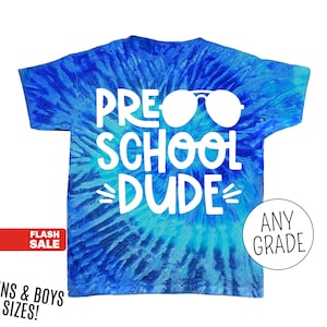 Op de afbeelding: Een blauw tie-dye t-shirt met de witte woorden "PRE SCHOOL DUDE" en een witte zonnebril. Het shirt heeft ook de woorden "ANY GRADE" in een cirkel. Het shirt is voor "MENS & BOYS SIZES!"