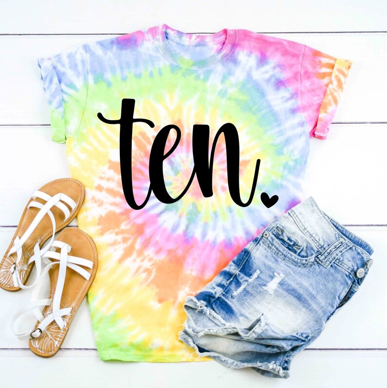 May include: A tie-dye t-shirt with the word "ten" in black script. The shirt is paired with denim shorts and sandals.